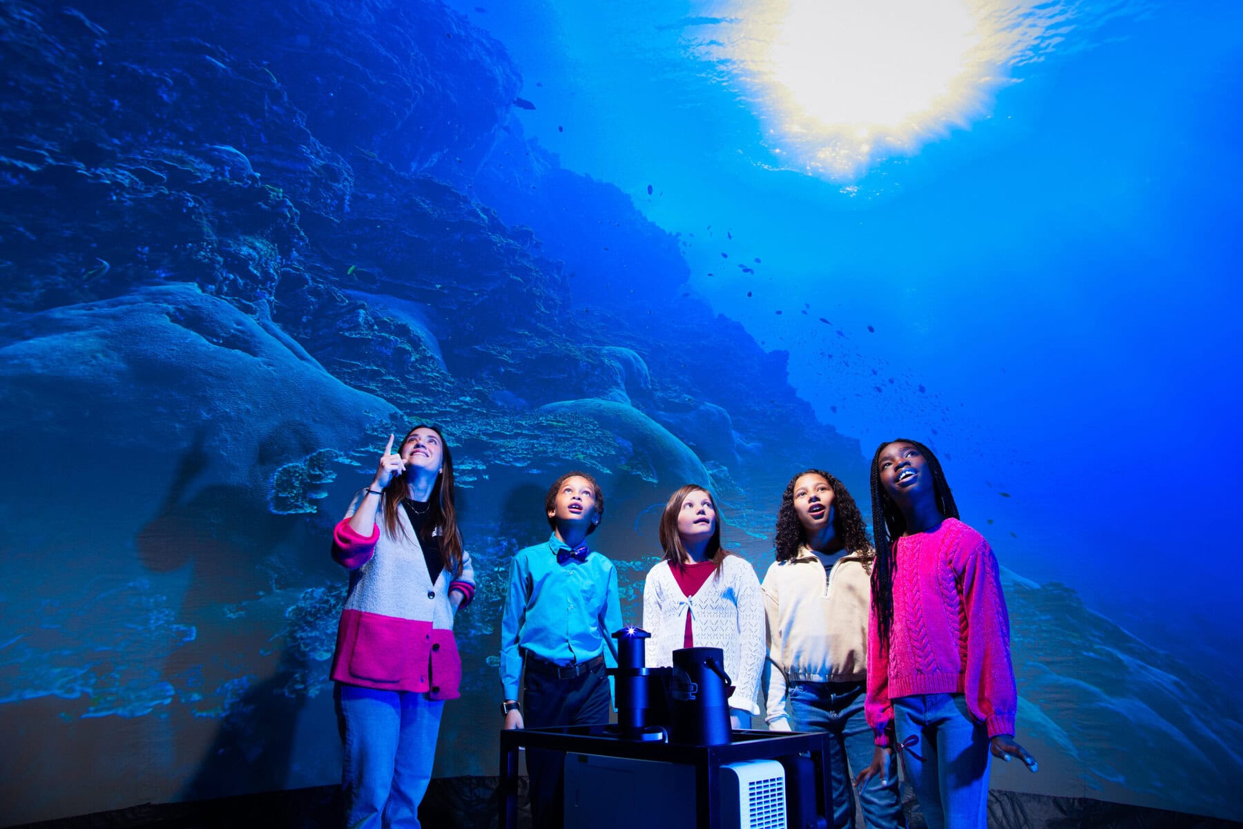 Students stand with a teacher and experience the underwater content inside a Starlab
