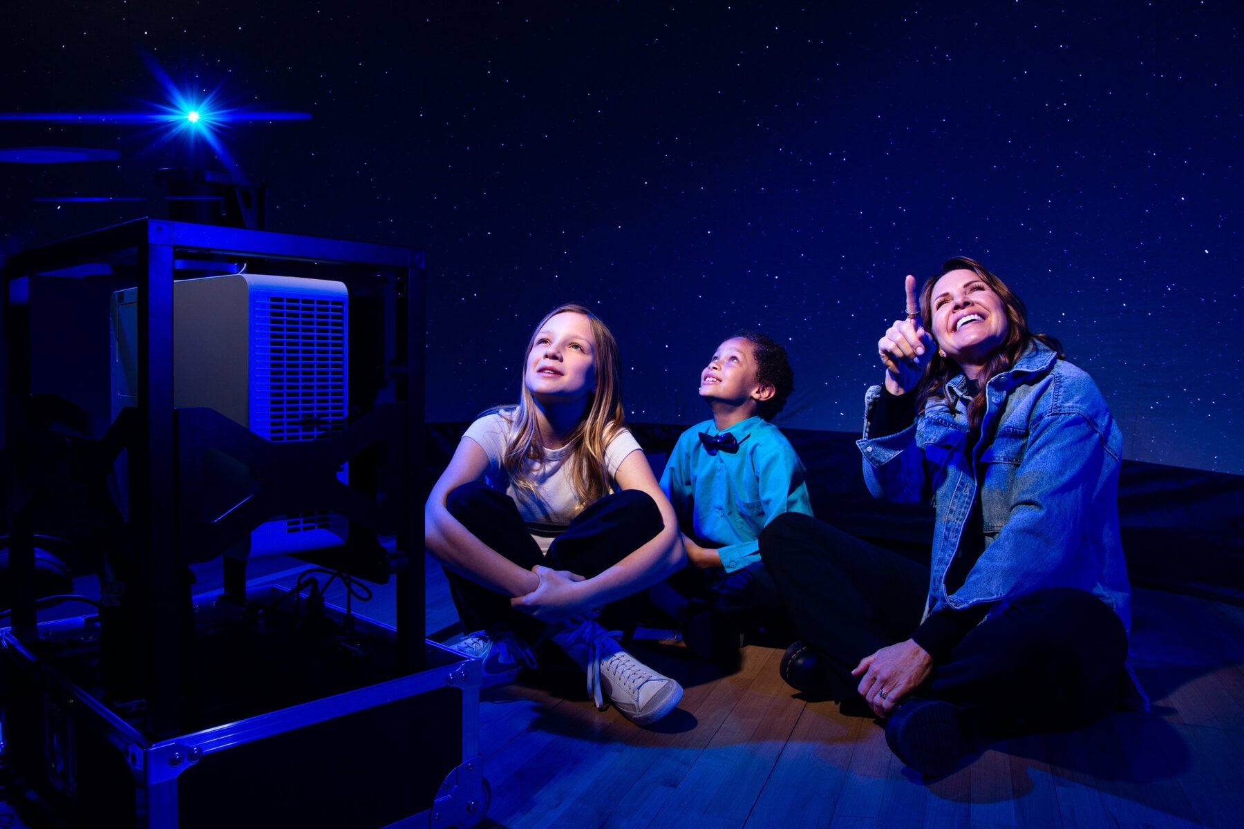 Students sit inside a Starlab with a teacher who points up to the content.